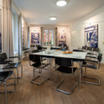 Das Bild zeigt den Ausstellungs- und Seminarraum im Bonhoeffer-Haus mit Informationstafeln, Stühlen und moderner Beleuchtung. The picture shows the exhibition and seminar room at the Bonhoeffer House with information panels, chairs, and modern lighting.